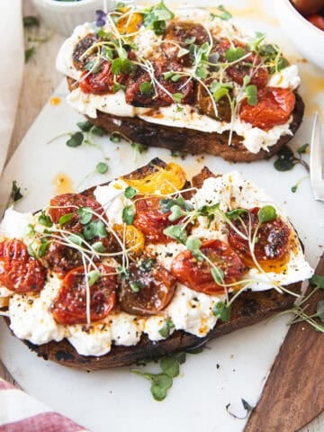 Close up overhead view of burrata toast topped with blistered mixed cherry tomatoes and micro greens on toasted sourdough