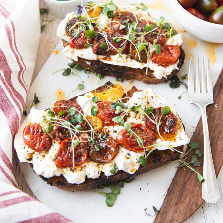 Close up overhead view of burrata toast topped with blistered mixed cherry tomatoes and micro greens on toasted sourdough