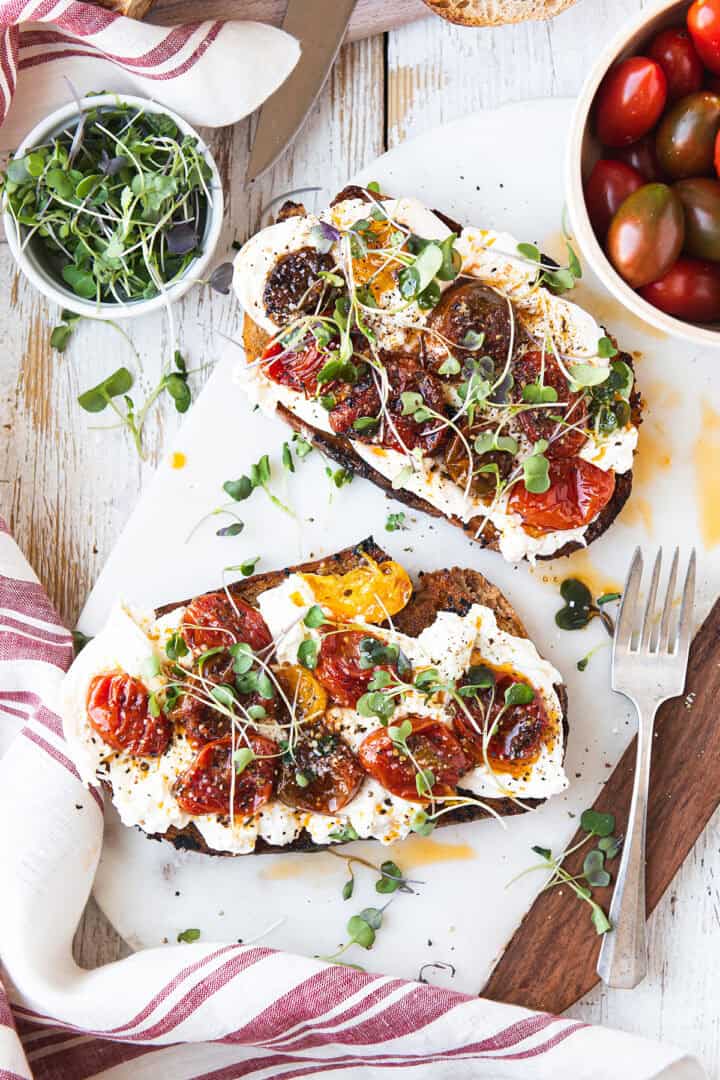 Burrata toast with blistered cherry tomatoes and micro greens on sourdough, served on a marble board