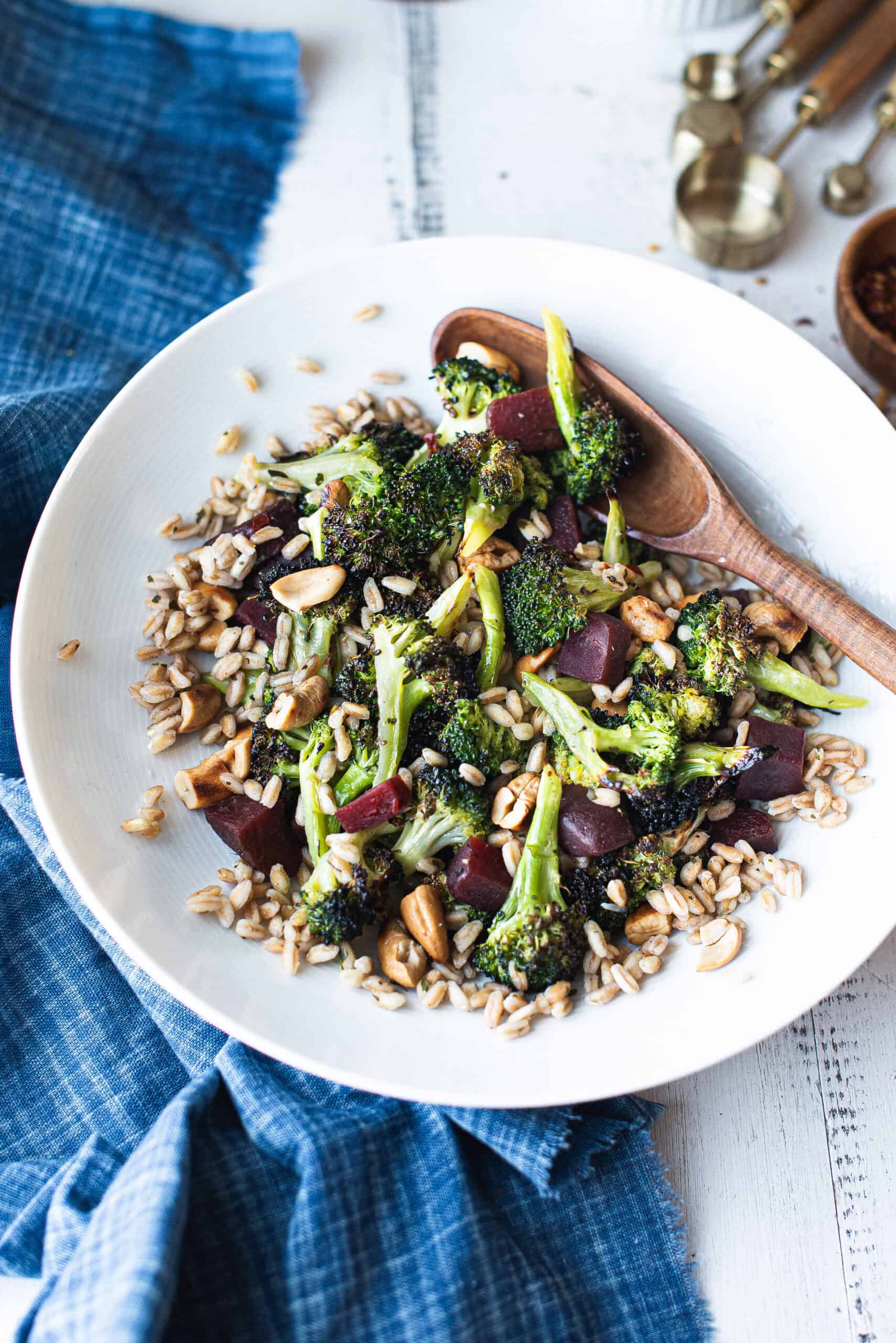 white bowl of broccoli salad with wooden serving spoon and blue napkin