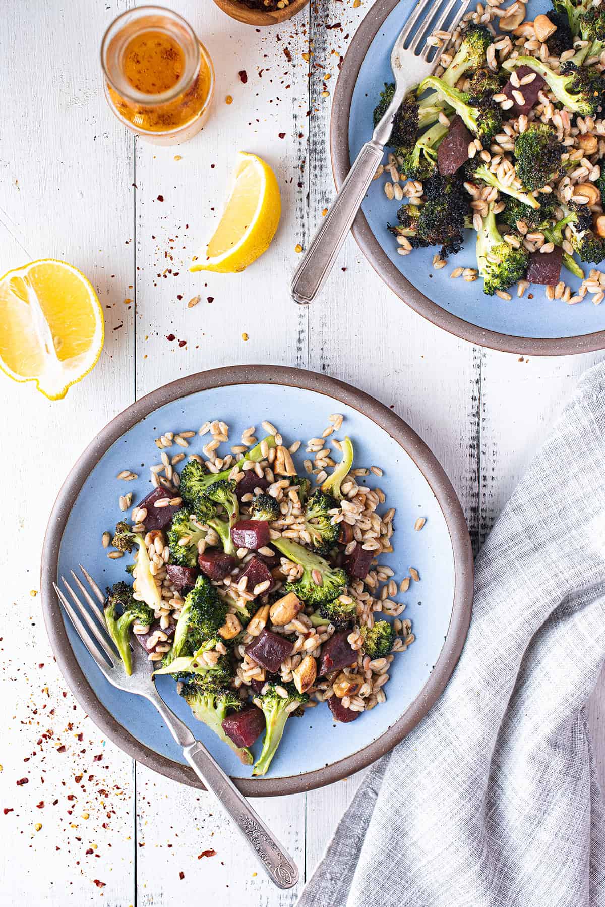 two blue plates with broccoli salad on white table with grey napkin and lemon wedges