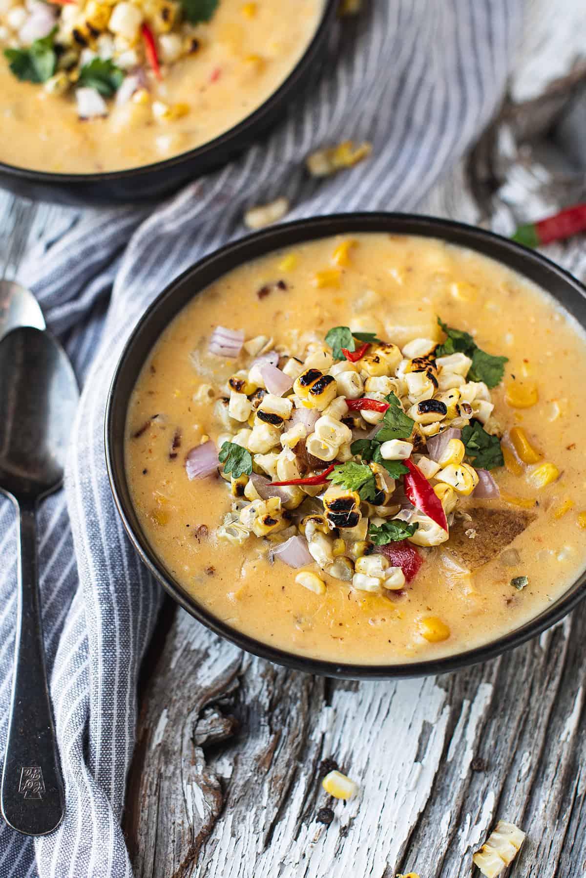 bowl of corn chowder topped with grilled corn and peppers + spoons