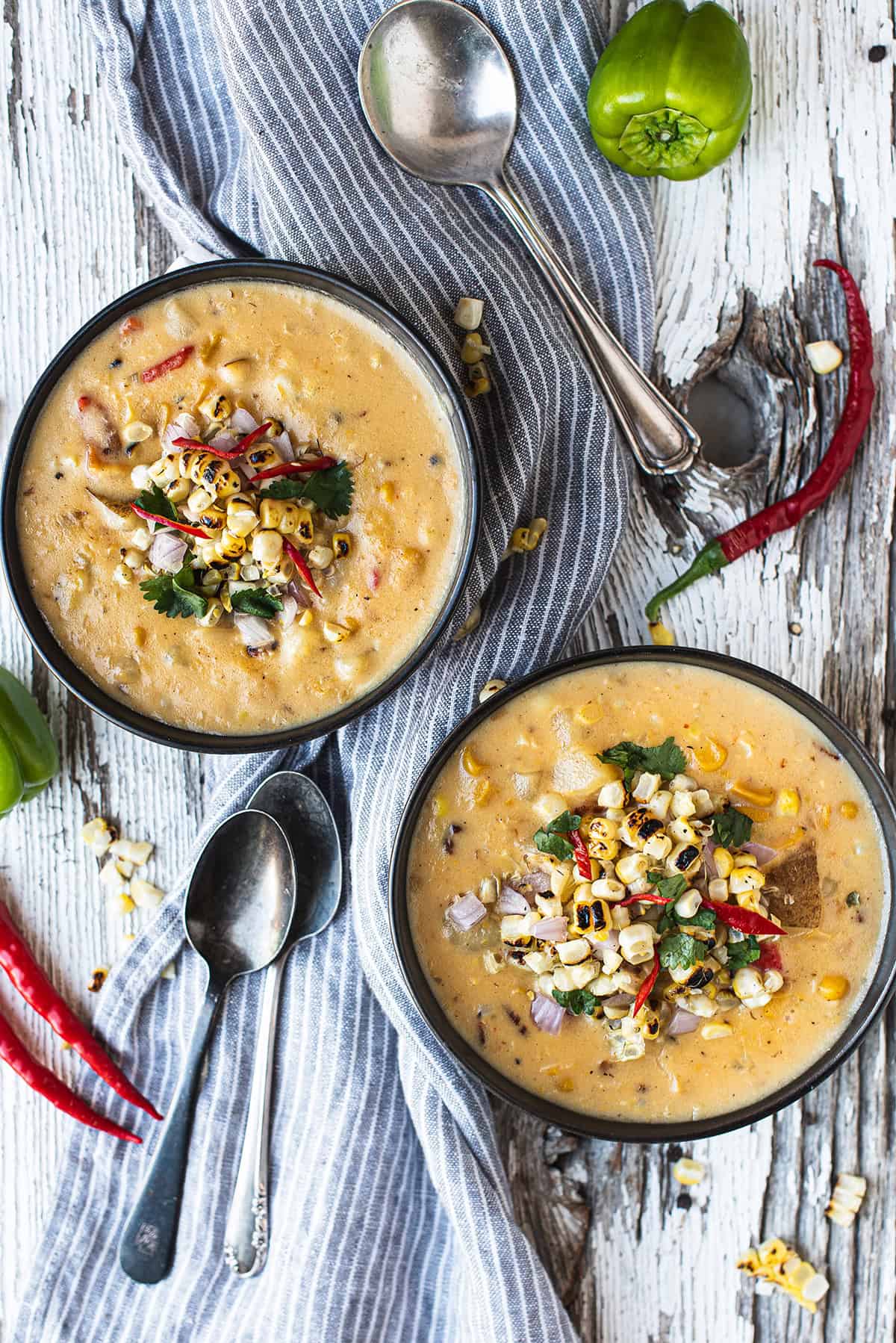 two bowls of corn chowder with blue napkin and spoons