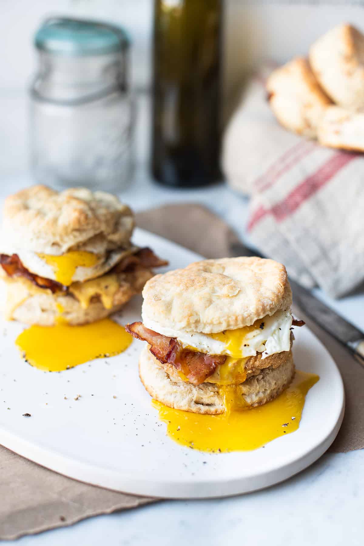 two chicken biscuit sandwiches with runny yolks on white plate