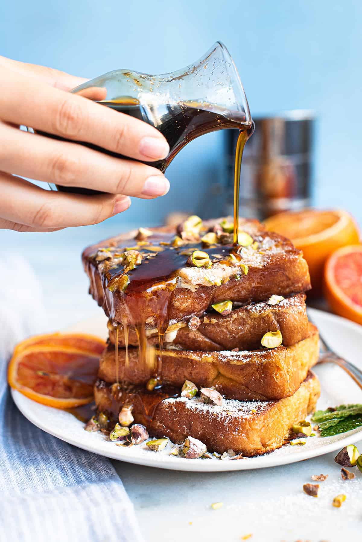 stack of French toast on white plate with hand pouring syrup over the top
