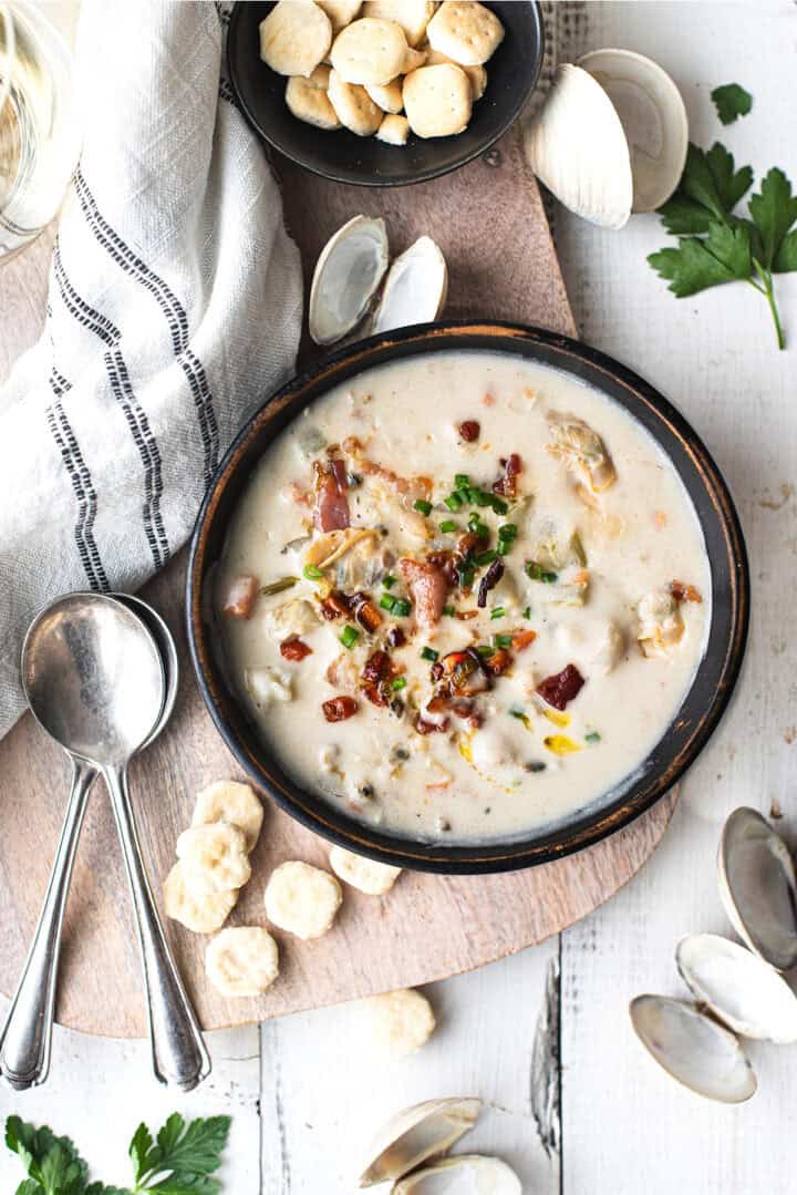 clam chowder in bowl with spoons, linen napkin, and oyster crackers