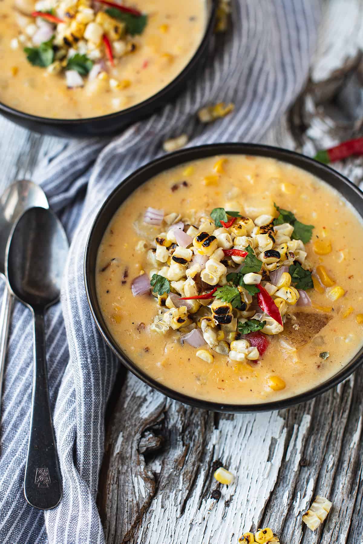 corn chowder in black bowl with corn kernels & peppers on top + spoons