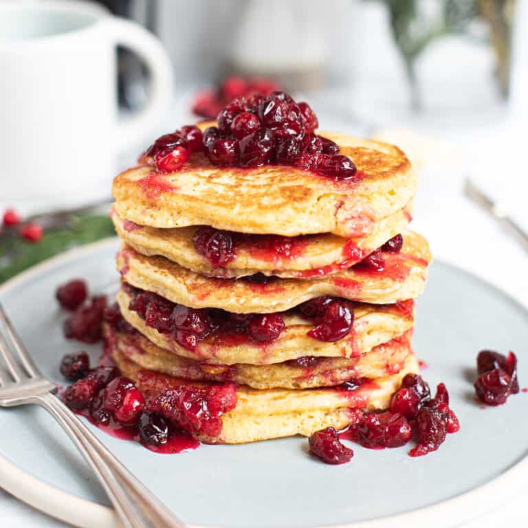 stack of cornmeal pancakes on blue plate with fork, topped with fresh cranberry compote