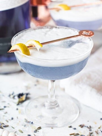 blue frost fizz gin cocktail in coupe glass garnished with lemon twist