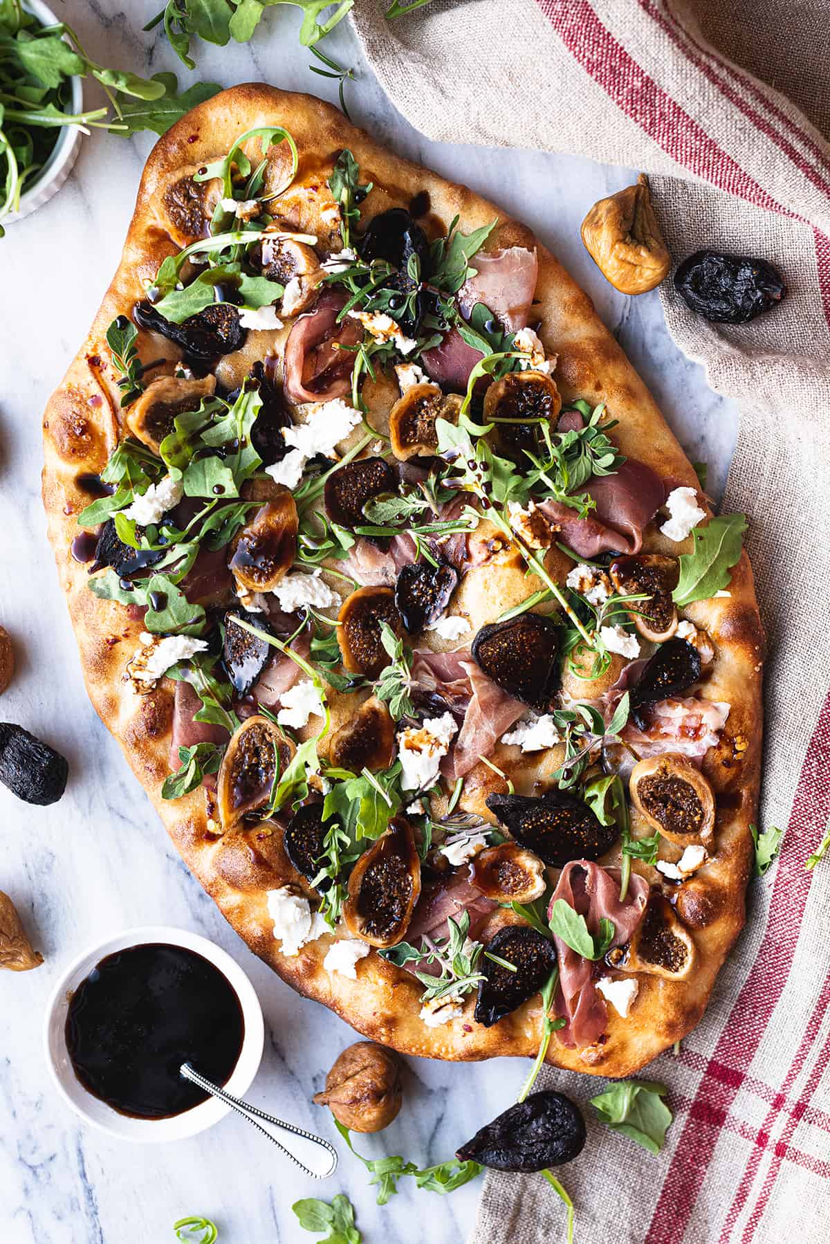 whole fig flatbread pizza on white surface with linen napkin and balsamic glaze