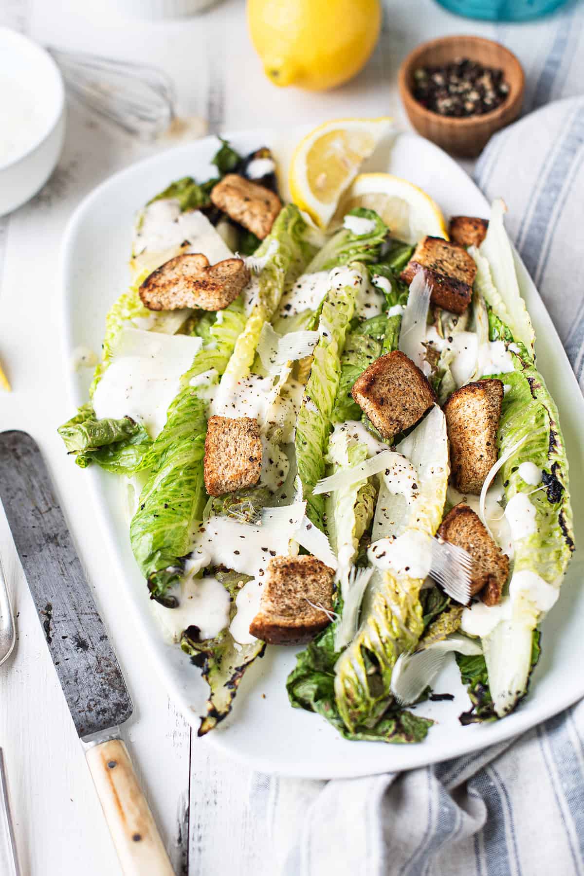 Close-up of grilled romaine Caesar salad with creamy homemade dressing, toasted croutons, and shaved Parmesan on a white serving platter