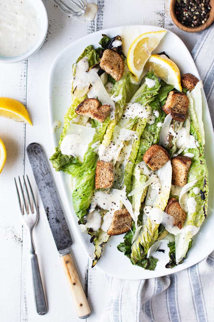 Grilled romaine Caesar salad on a white platter with homemade Caesar dressing, croutons, and shaved Parmesan