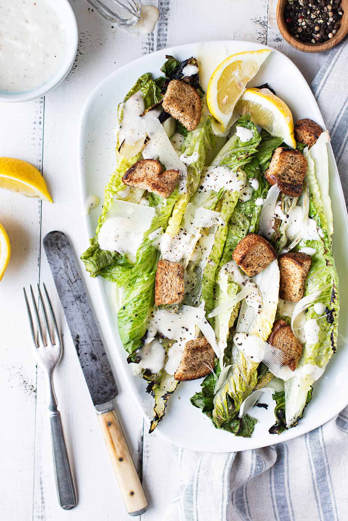 Grilled romaine Caesar salad on a white platter with homemade Caesar dressing, croutons, and shaved Parmesan
