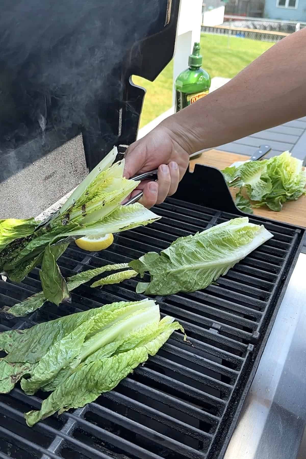 Romaine lettuce halves charring on a hot gas grill with visible grill marks and steam