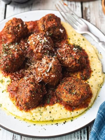meatballs stacked on plate, served over polenta with red sauce on top,