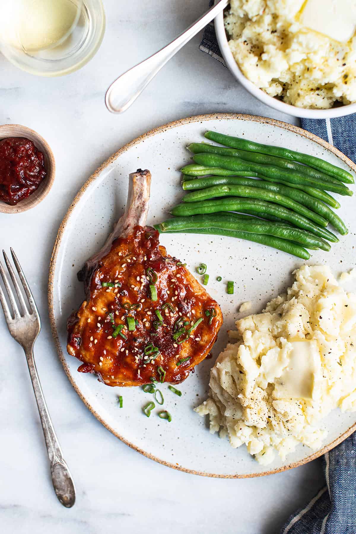 Korean glazed pork chop on white plate with green beans and mashed potatoes + fork