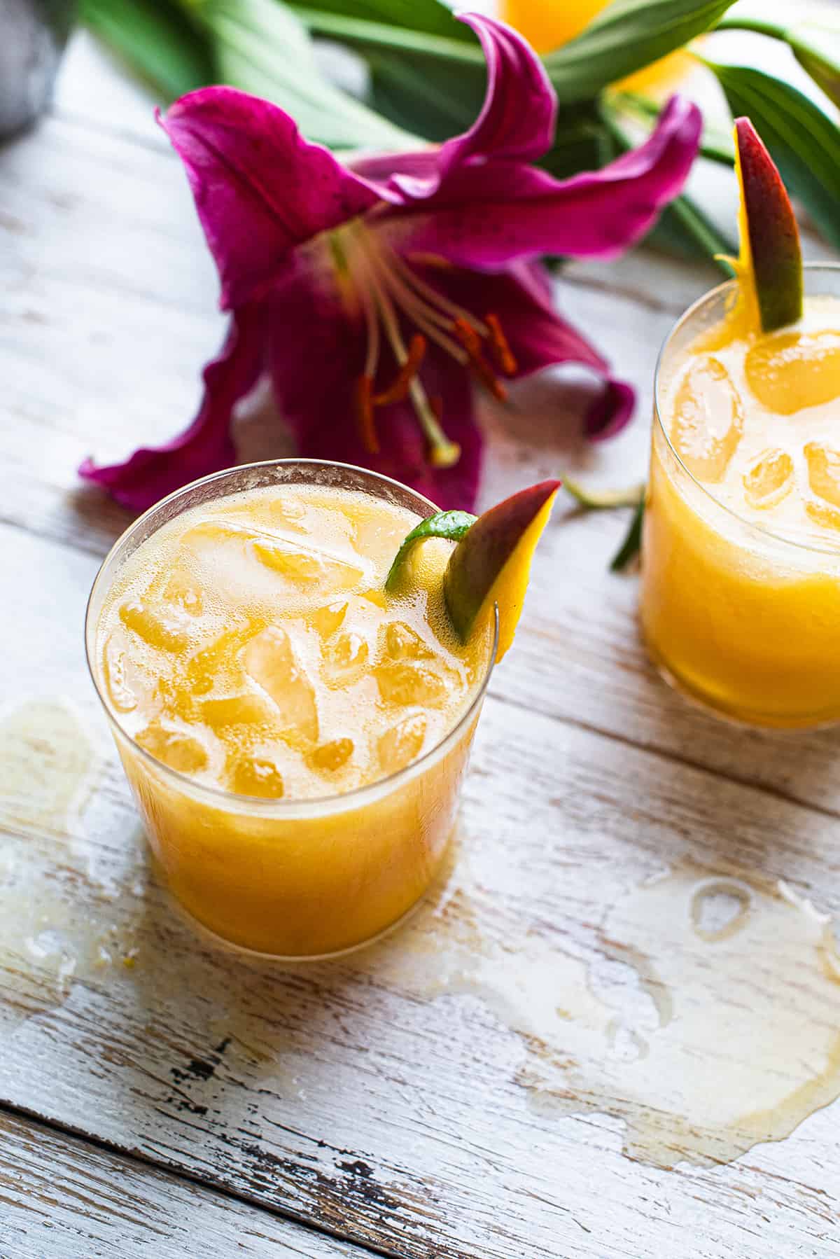 two orange mango cocktails with pink orchid on white wood