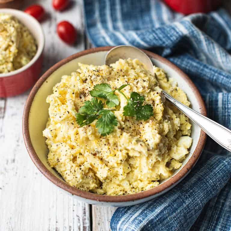 one large bowl of mashed potato salad with spoon, garnished with parsley and blue napkin