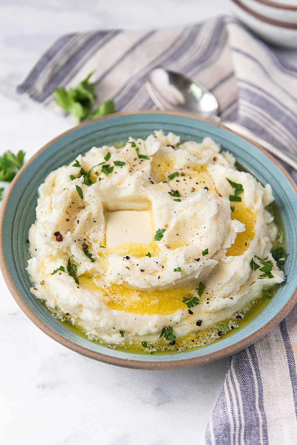 bowl of creamy mashed potatoes with melted pools of butter and blue striped napkin