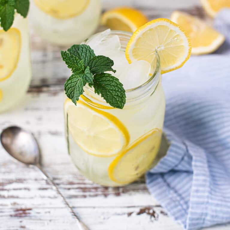 mason jar filled with lemonade on white table, garnished with lemon slices and mint leaves + blue napkin and spoon