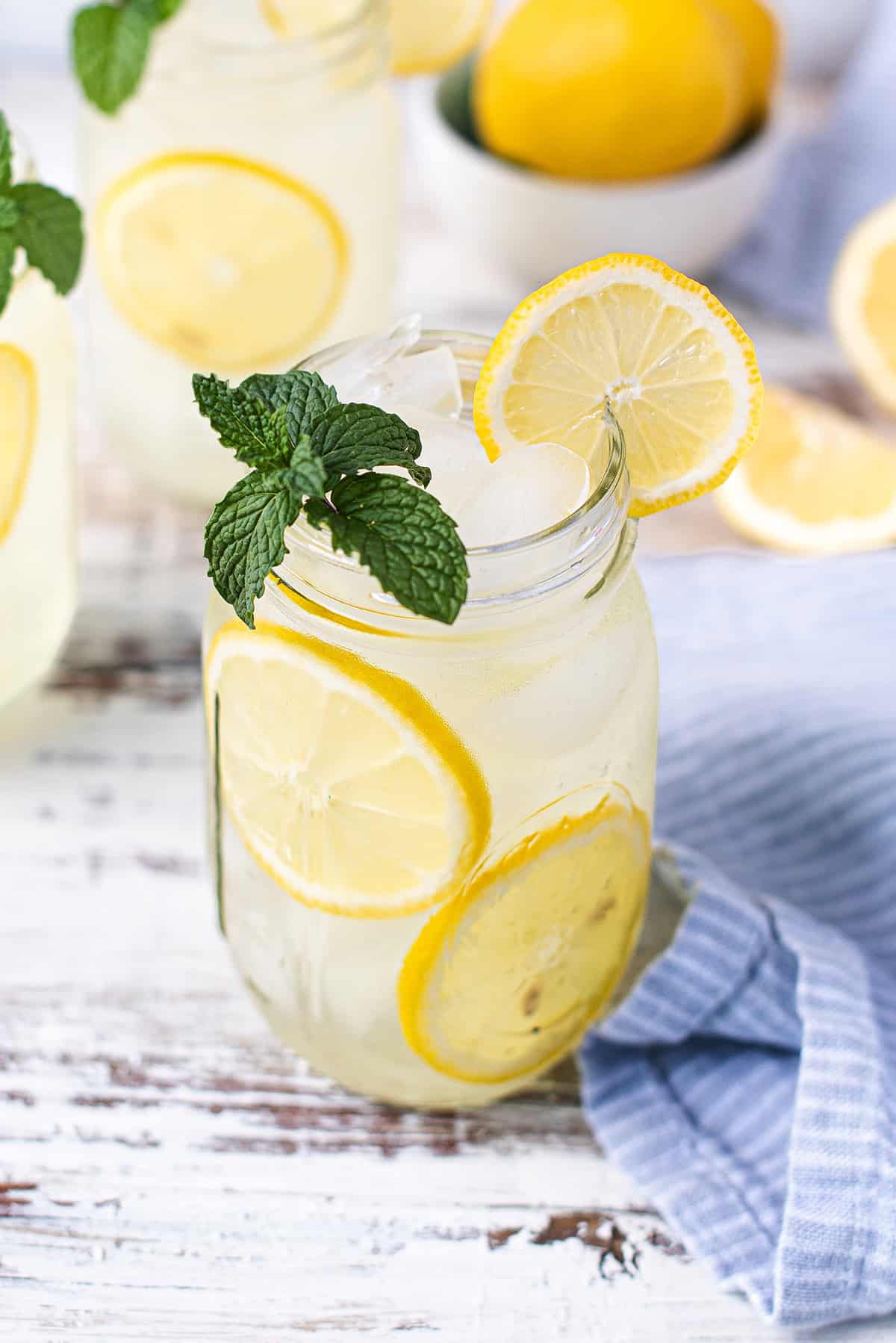 white picnic table with 3 mason jars of mint lemonade, garnished with lemon wedges and mint leaves