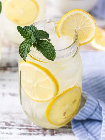 mason jar filled with lemonade on white table, garnished with lemon slices and mint leaves + blue napkin and spoon