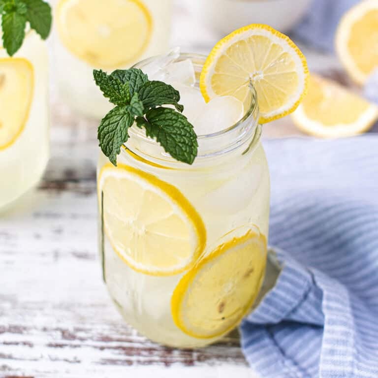 mason jar filled with lemonade on white table, garnished with lemon slices and mint leaves + blue napkin and spoon