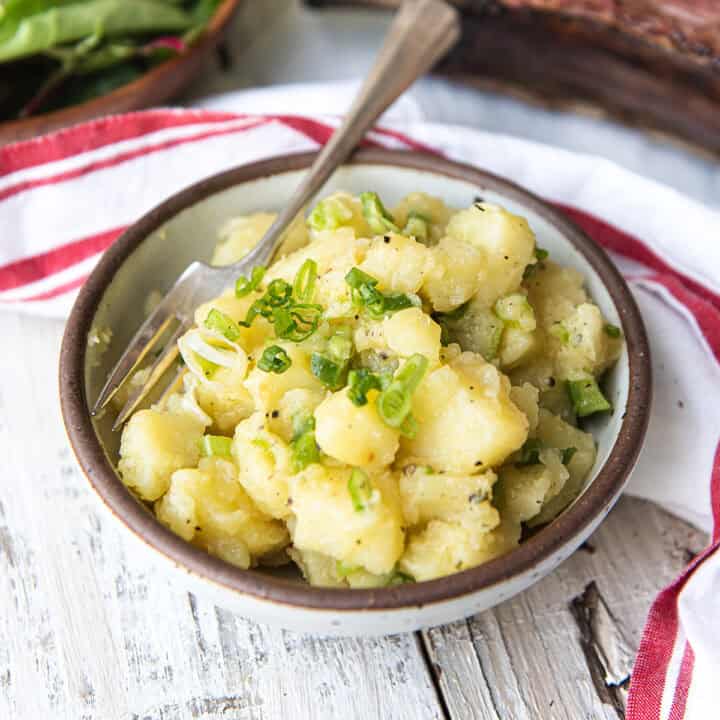 white bowl of old fashioned potato salad with spoon + red striped napkin