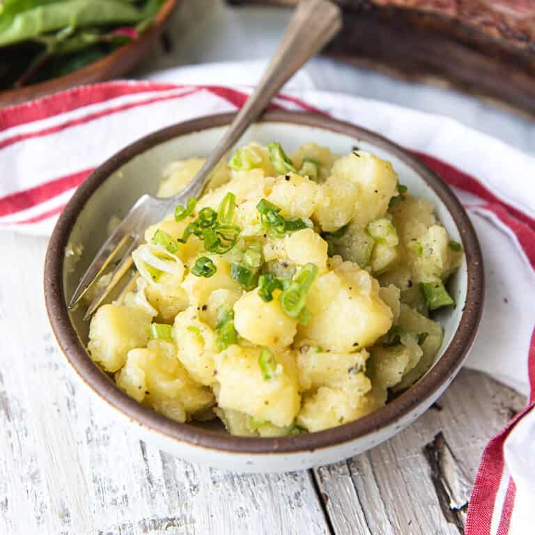 white bowl of old fashioned potato salad with spoon + red striped napkin