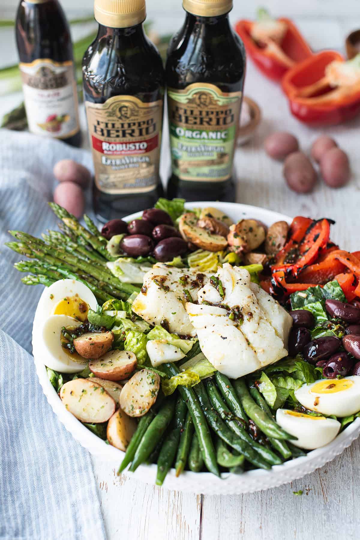 finished bowl of olive oil poached cod salad with herbs and colorful vegetables