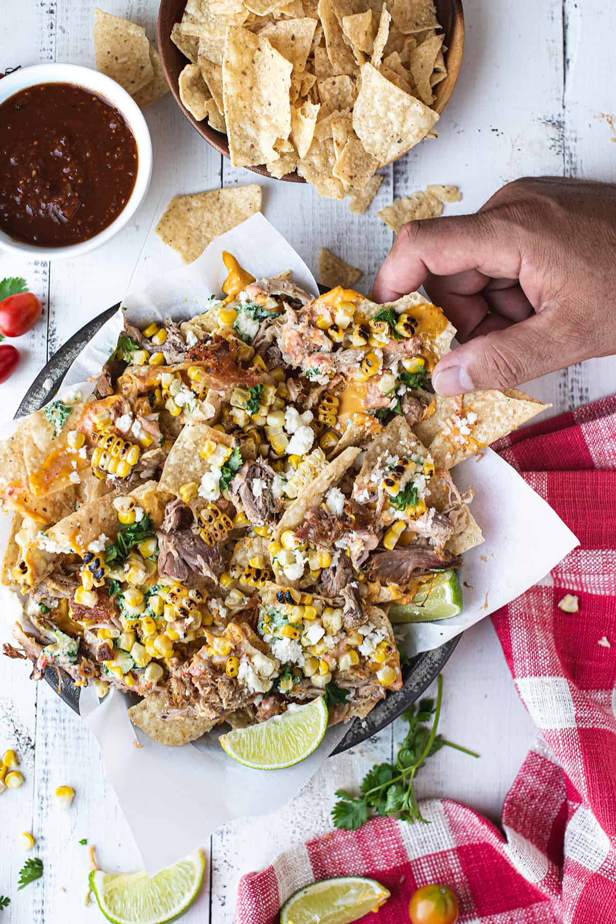 hand grabbing loaded pork nachos in pan with white paper 
