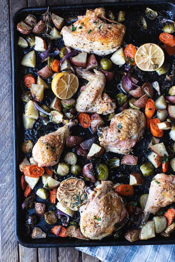 roasted chicken breasts, thighs, and wings on sheet pan with chopped colorful vegetables, garlic, and lemon wedges