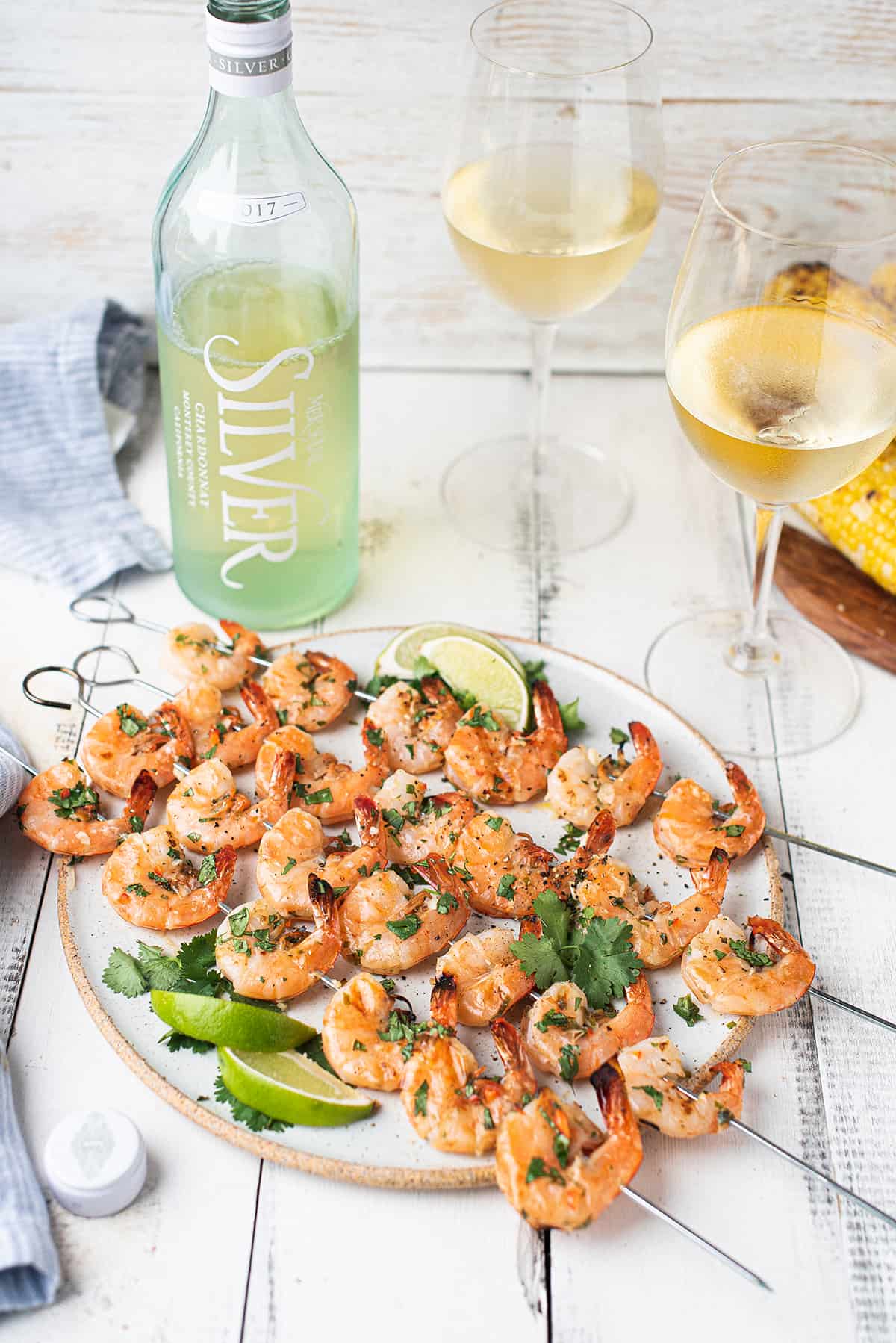 shrimp skewers on white plate with glasses & bottle of white wine