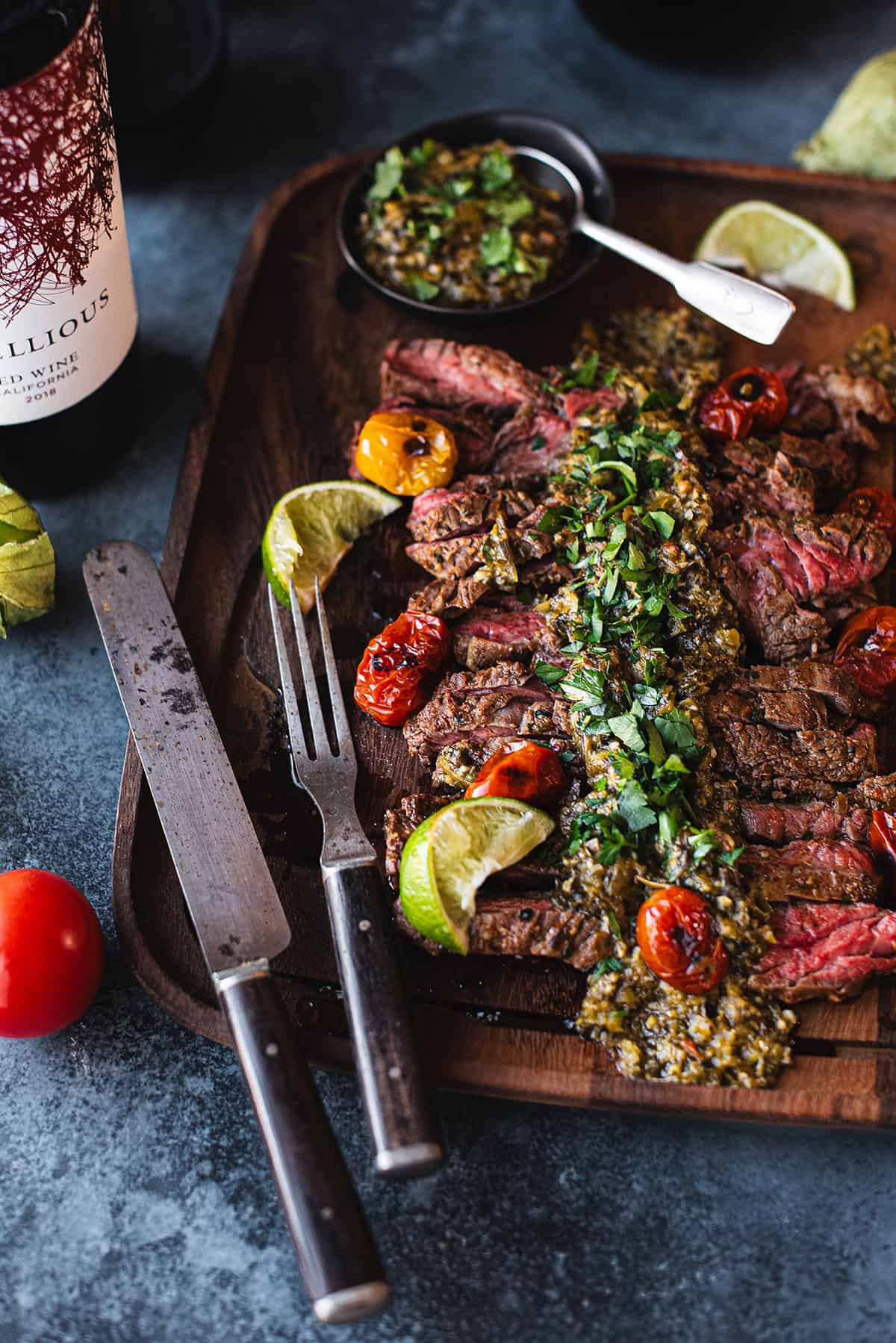 skirt steak on wood platter with fork & knife + chimichurri on top