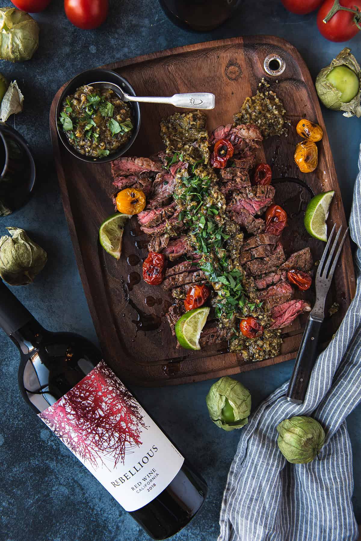 skirt steak on wood platter, chimichurri on top with rebellious wine