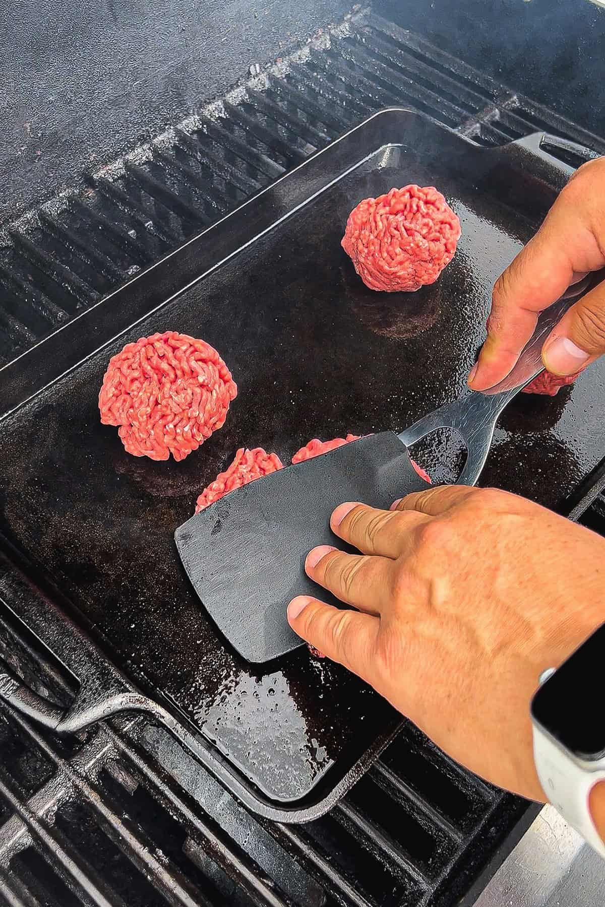 Keith pressing beef balls into thin patties on a cast iron grill pan using spatula