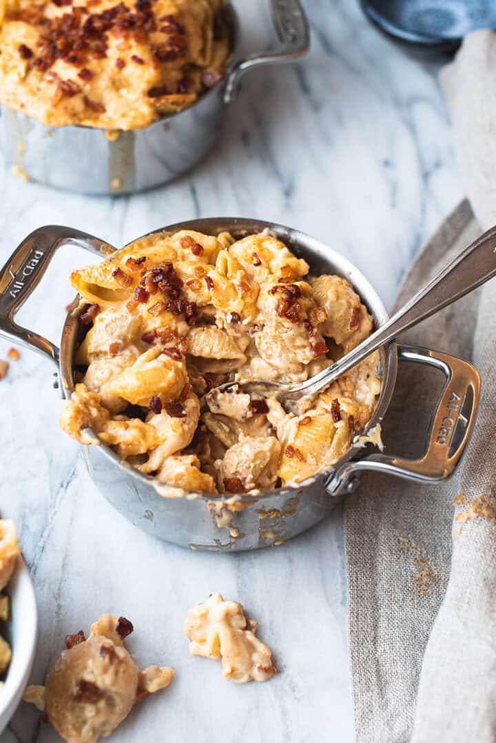 small stainless steel pan of mac and cheese, partially eaten, with spoon on marble table