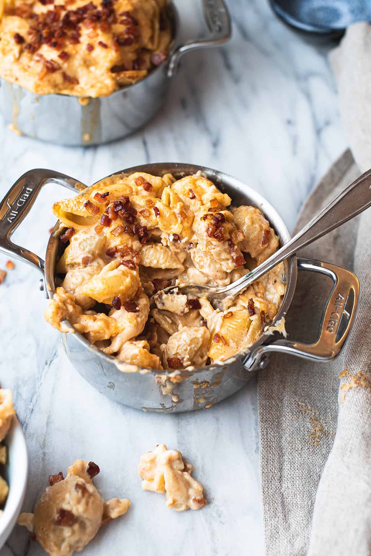 small stainless steel pan of mac and cheese, partially eaten, with spoon on marble table