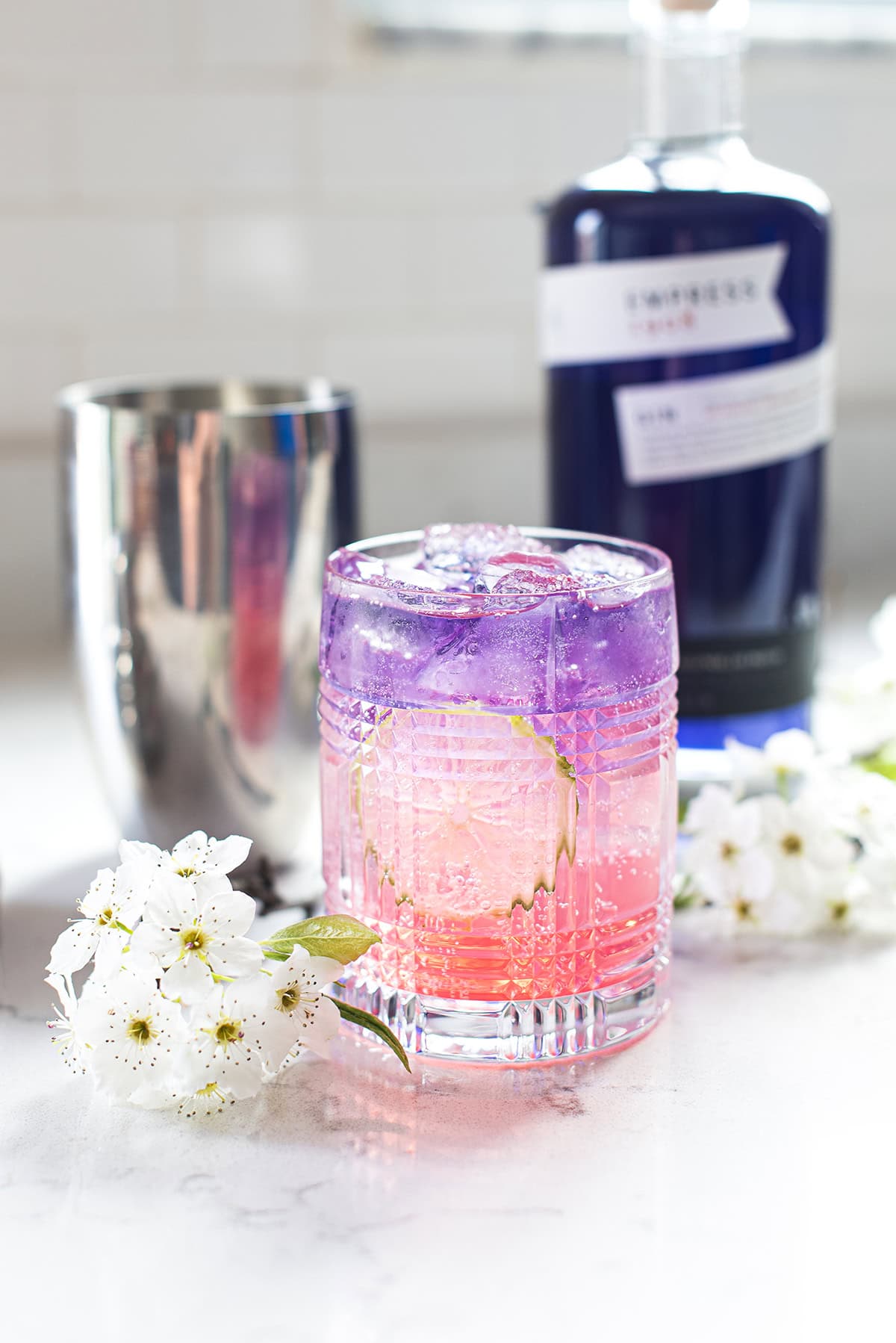 blue & pink empress gin cocktail on white countertop with gin bottle in backgound
