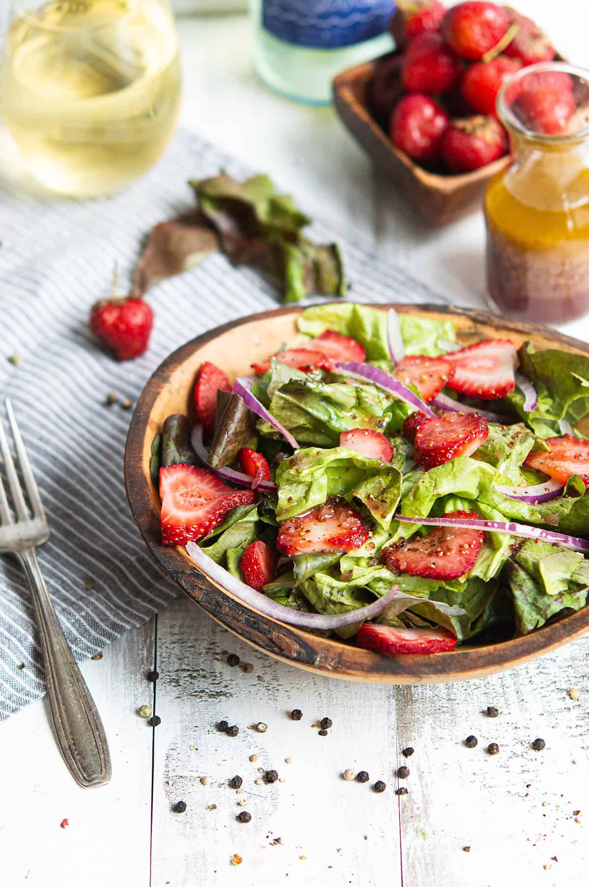 close-up of strawberry salad with red onion and leaf lettuce in a wooden bowl, with a glass of sparkling wine in the background