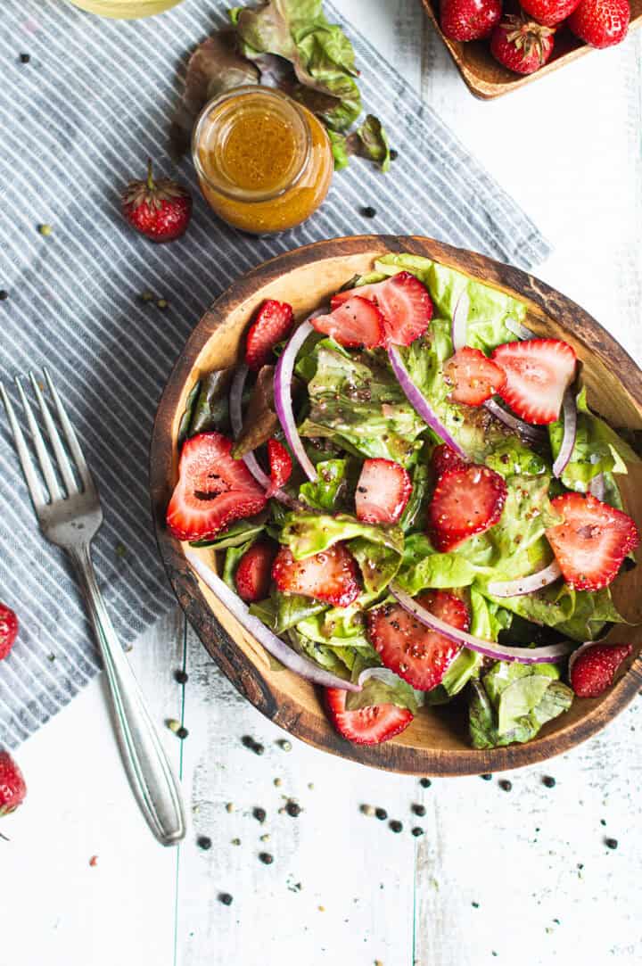 strawberry salad recipe with sliced strawberries, red onion, and lettuce in a rustic wooden bowl