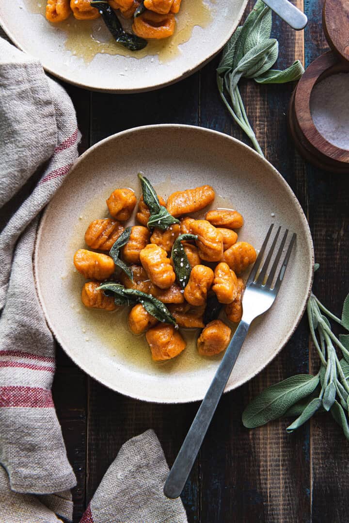 sweet potato gnocchi on ivory plate garnished with sage + fork