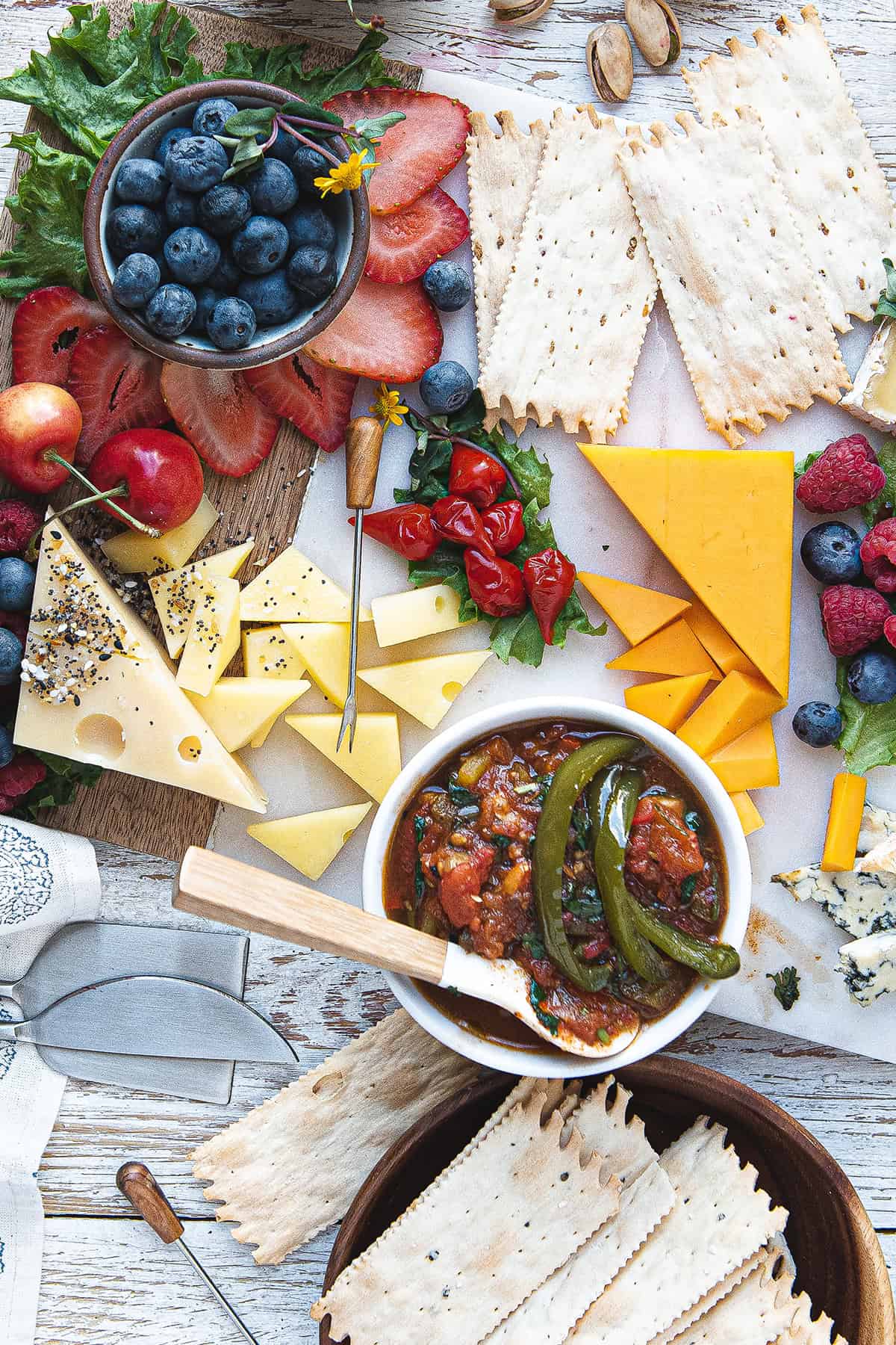 A table with a variety of cheeses, fruit, and tomato jalapeno jam on it.