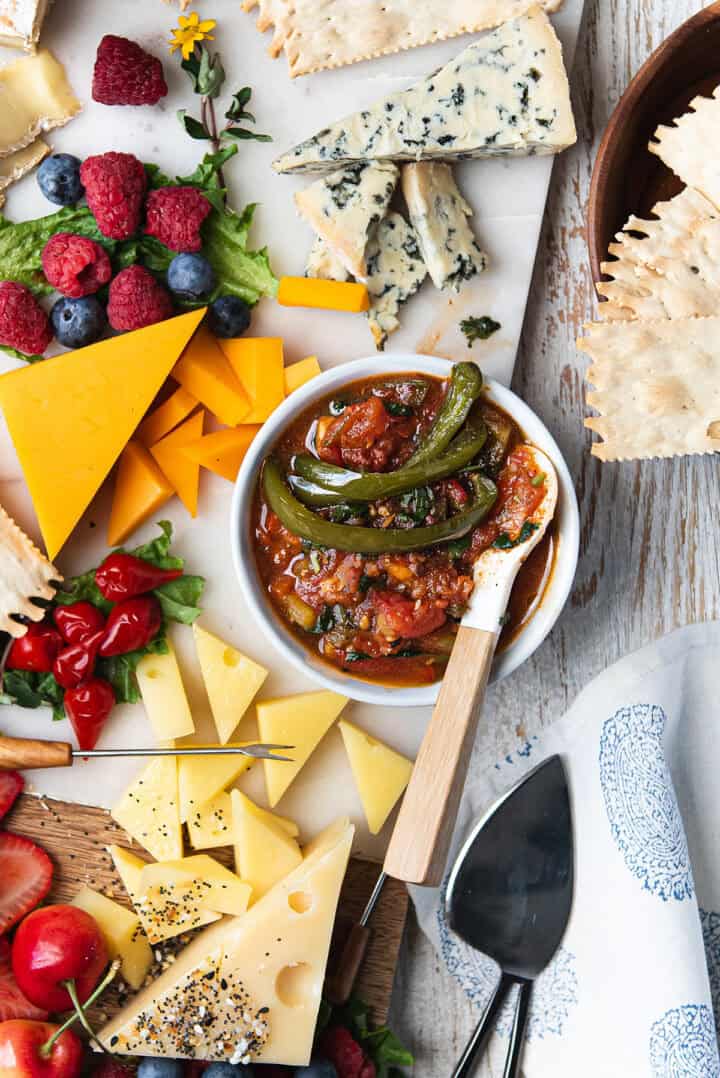 A table topped with tomato jalapeno jam, cheese, crackers, and vegetables.