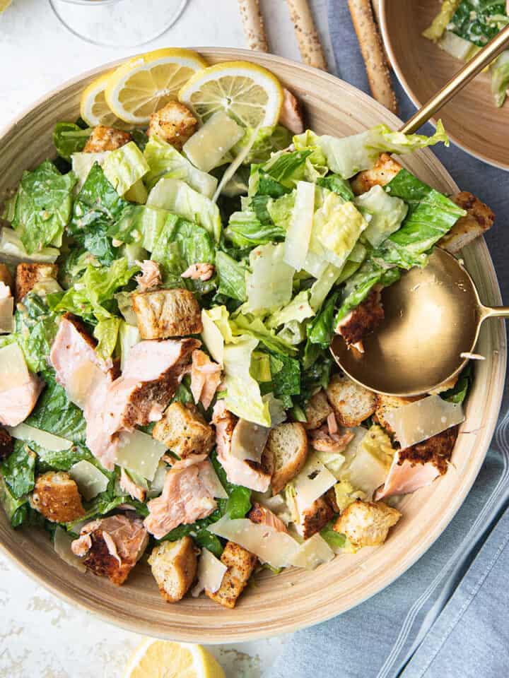 Large wooden bowl of Caesar salad with gold serving spoons
