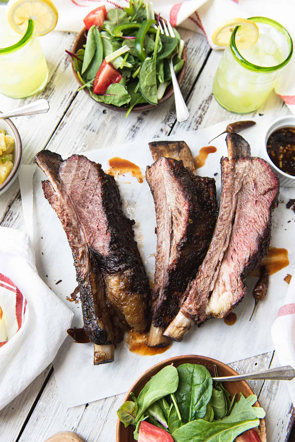 smoked beef ribs on parchment paper with salads red striped napkin, lemonade
