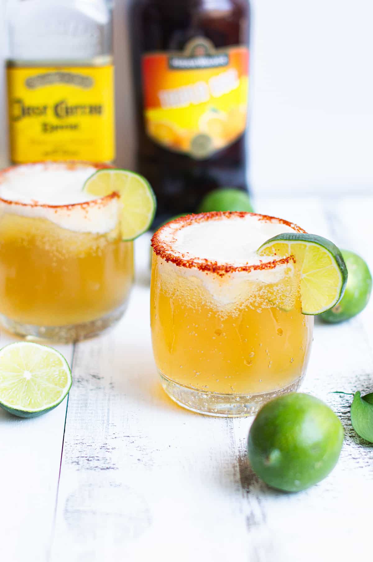 two beer margaritas on white table, garnished with lime with bottles and limes in background