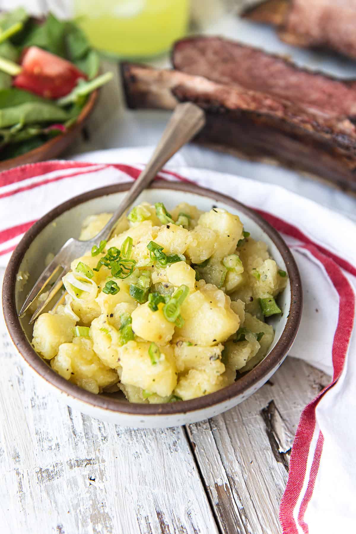 white bowl of old fashioned potato salad with spoon + red striped napkin