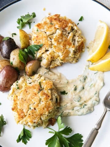 two crab cakes on white plate with lemon aioli + fork