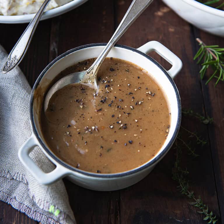 A small white saucepan filled with homemade beef gravy, topped with cracked black pepper